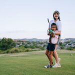 A mother and daughter laughing together as they play a round of golf outdoors on a sunny day