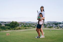 A mother and daughter laughing together as they play a round of golf outdoors on a sunny day