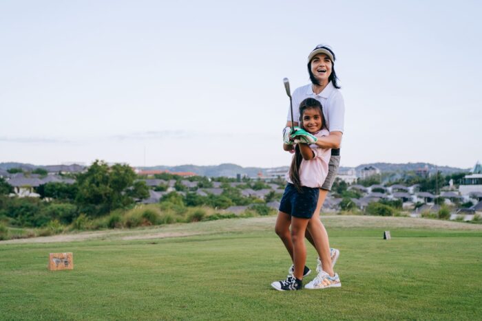 A mother and daughter laughing together as they play a round of golf outdoors on a sunny day
