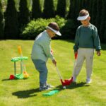 Two young children playing outdoor mini golf together with colourful putters in a sunny park