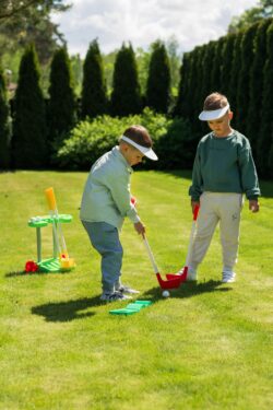 Two young children playing outdoor mini golf together with colourful putters in a sunny park