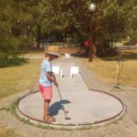 A child putting on an outdoor mini golf course in a sunny park