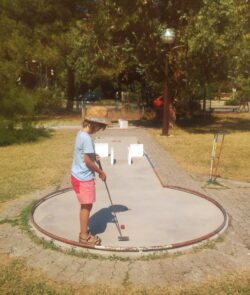 A child putting on an outdoor mini golf course in a sunny park