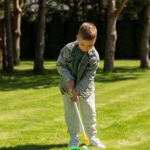 A young boy playing mini golf with a putter and ball on a sunny park lawn