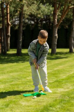 A young boy playing mini golf with a putter and ball on a sunny park lawn