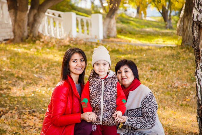 A grandmother, mother and young girl smiling together in a park on a golden autumn day